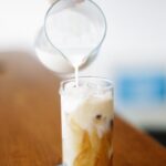 hand pouring milk into coffee