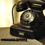 black rotary telephone beside ball pen on white printed paper