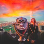 woman standing beside silver coin operated scope